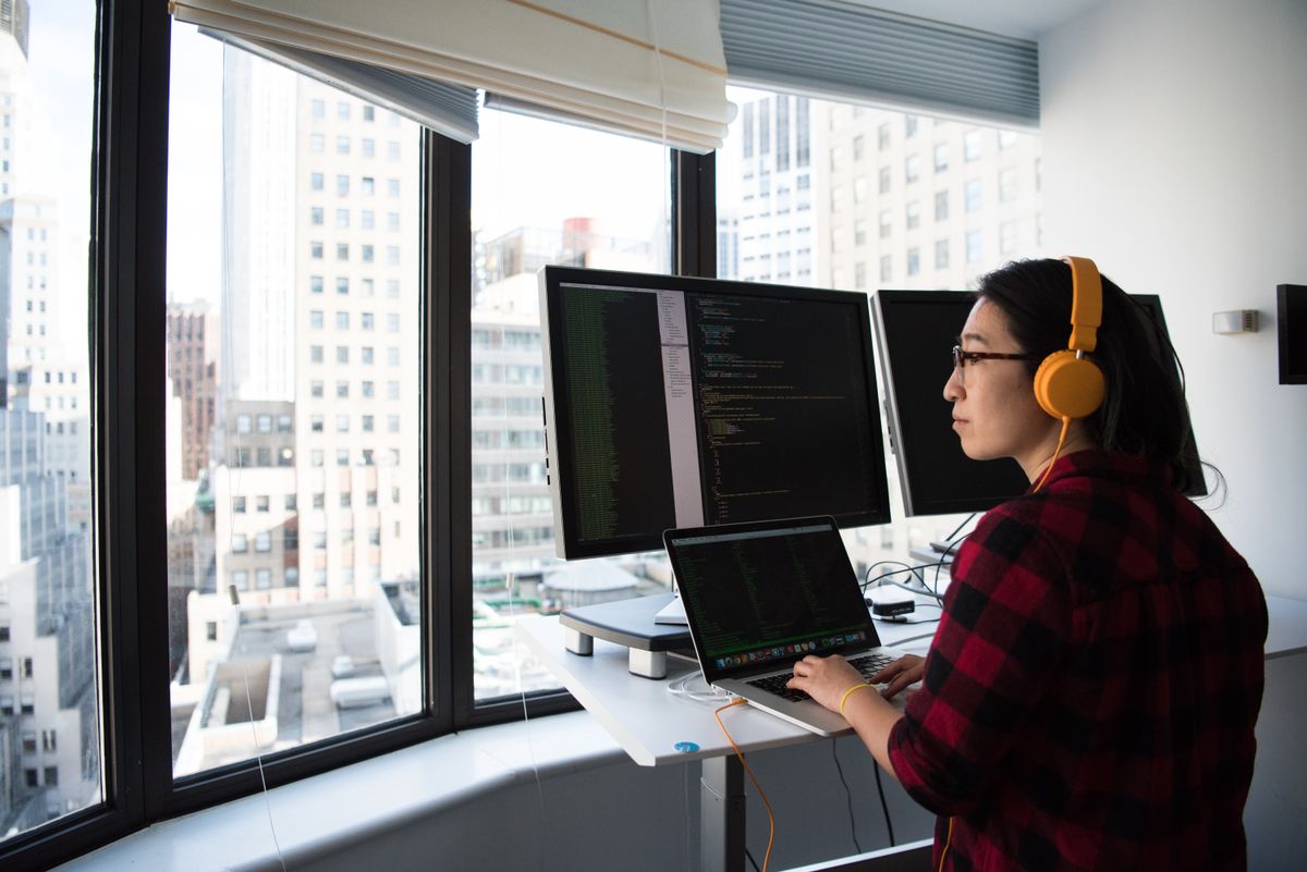 Deep-focus work at a standing desk, headphones on, code on the monitors