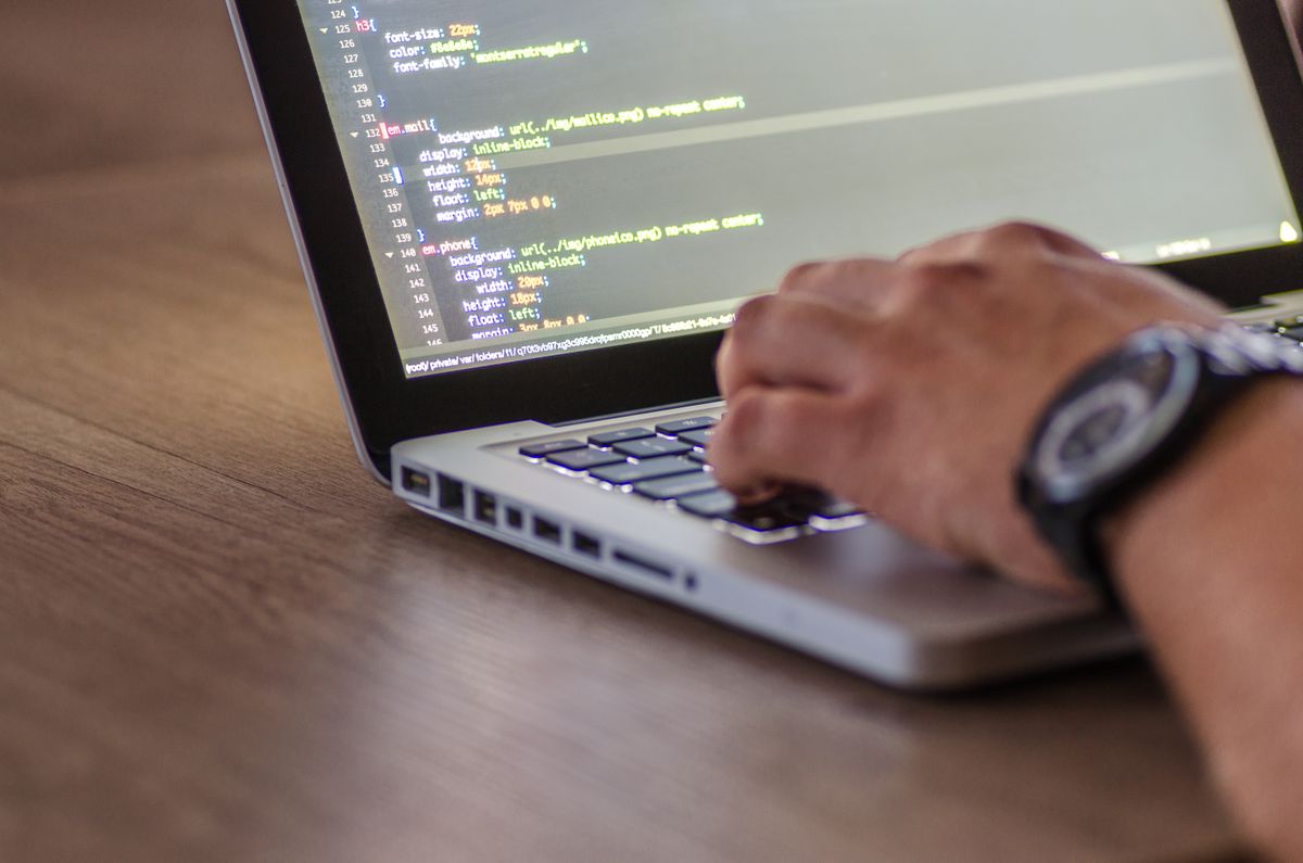 Hands editing stylesheet code on a laptop at a warm wooden desk